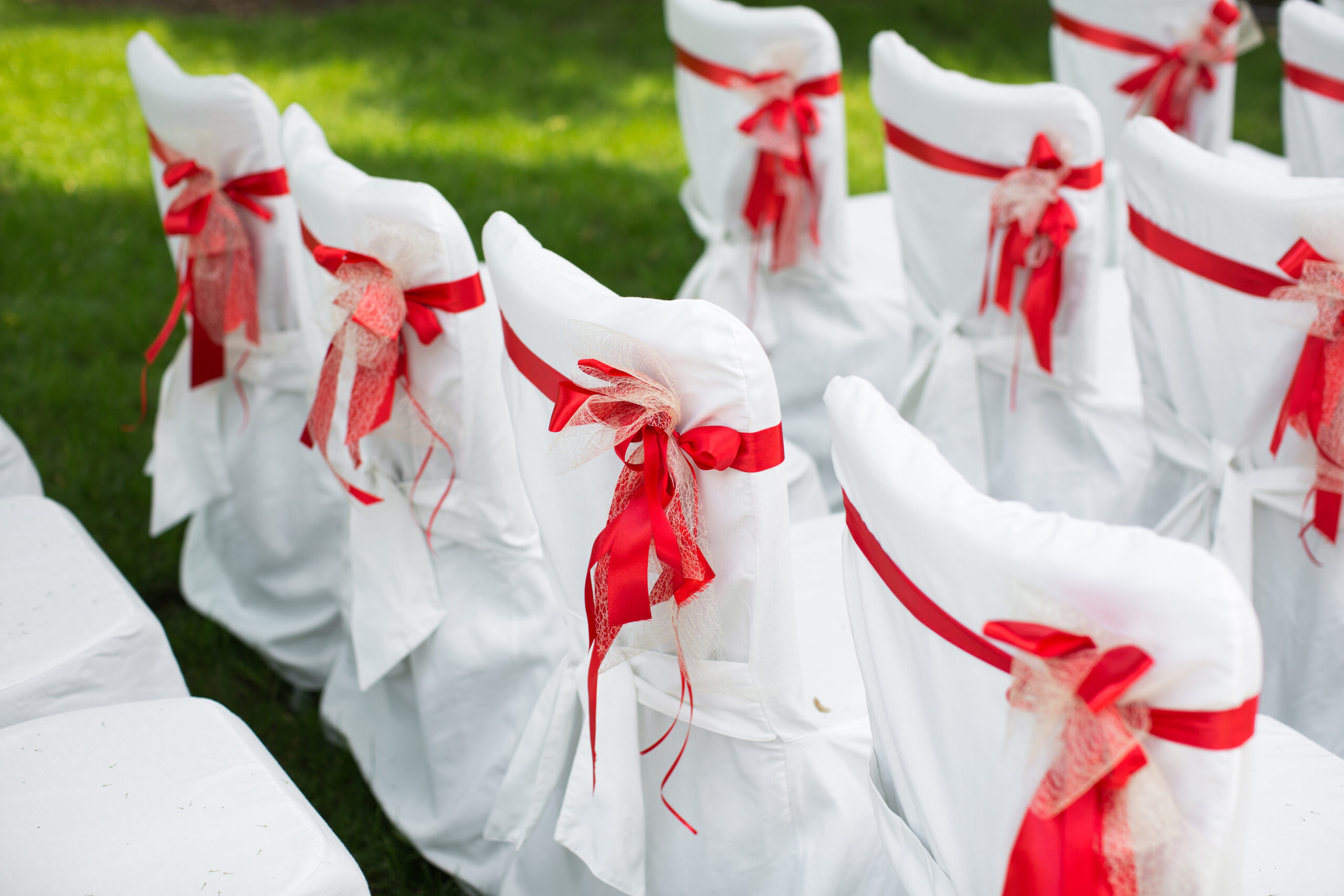 Wedding ceremony outdoors. White chairs with red ribbon.